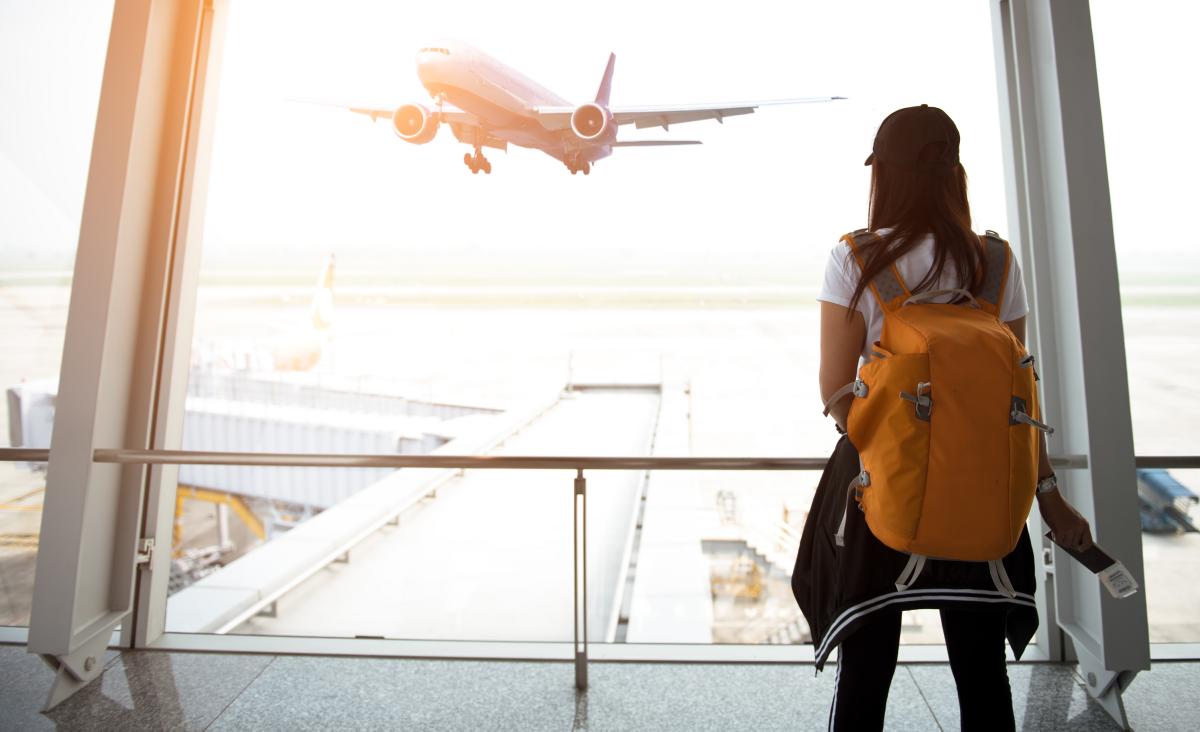 Traveler woman see the airplane at the airport window - Stopovers Paid By Carrier